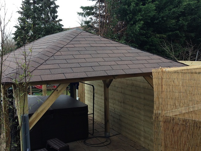 Large open sided gazebo in a garden in Weybridge, Surrey. The structure is covered with brown felt roof shingles for awtertight finish.
